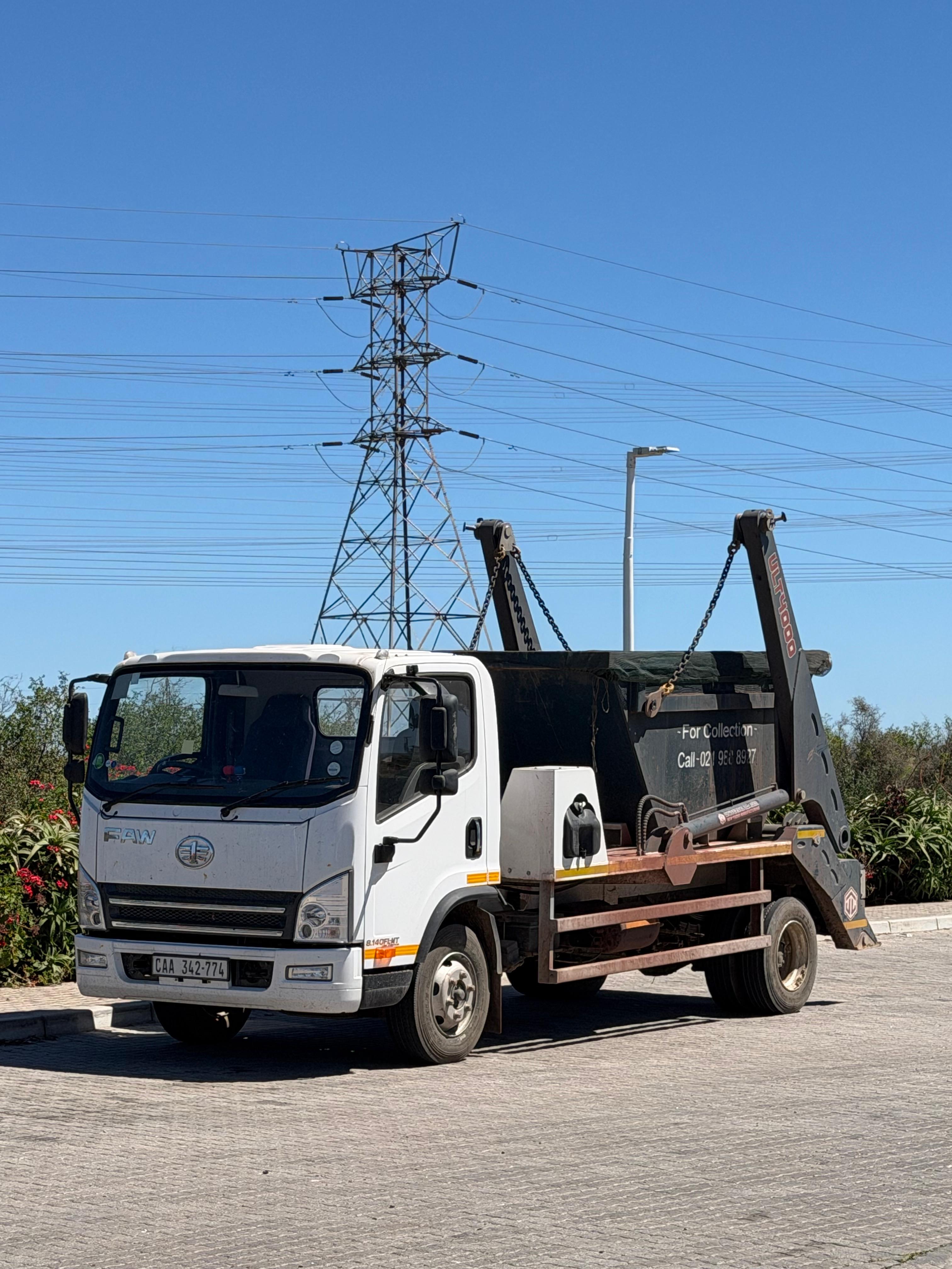 West Coast Skips hook-lift truck carrying a covered specialist skip at an industrial site